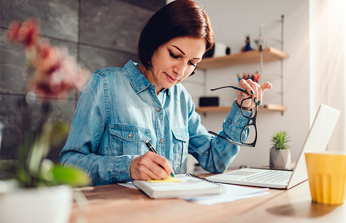 Woman writing notes in note pad and holding eyeglasses