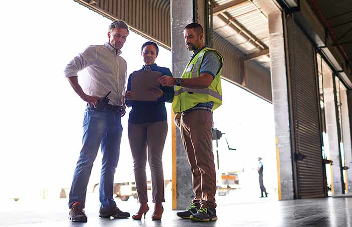 Three People Talking Shipping and Logistics in Warehouse