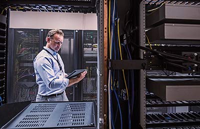 Man in Server Room Looking at Tablet