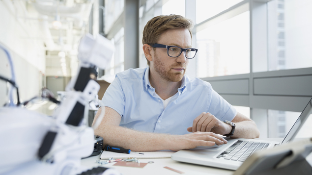 Engineer looking at laptop with robot