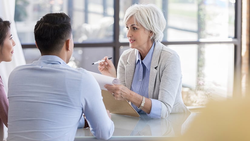 A senior woman sits at a table and talks with young woman