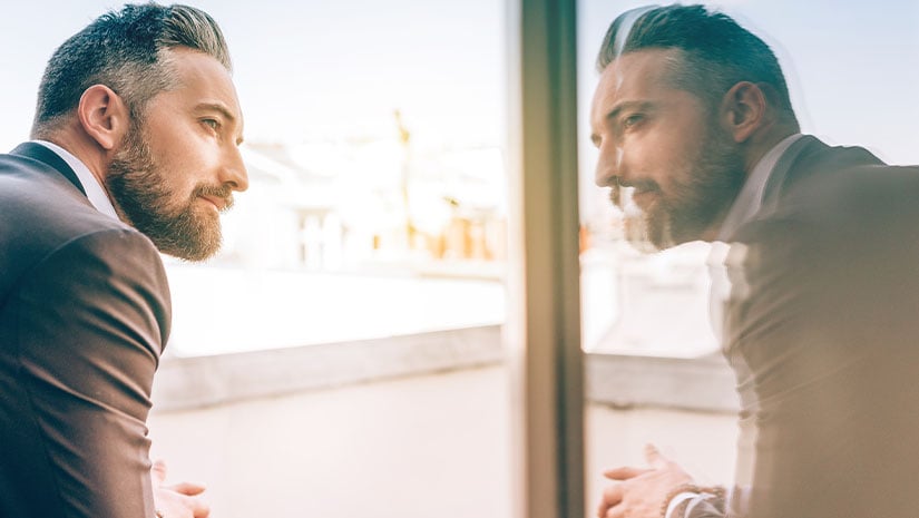 Bearded business man reflecting himself in window glass