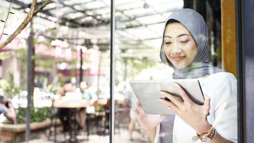 Elegant Muslim business woman working on a tablet through glass