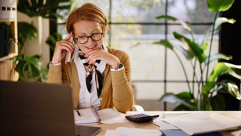 Happy businesswoman using mobile and laptop while working at home