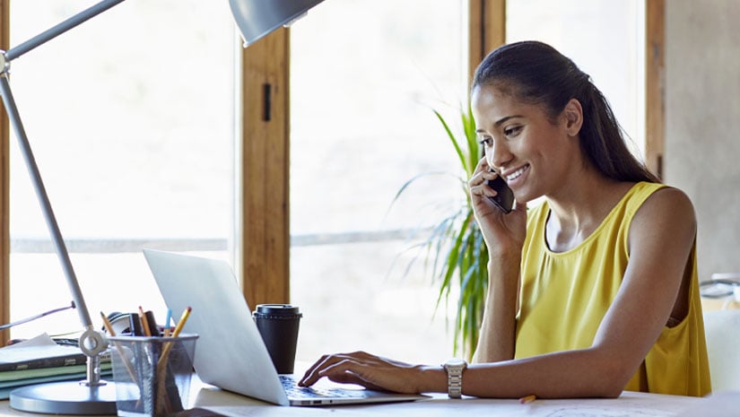 Happy businesswoman using cell phone and laptop in office
