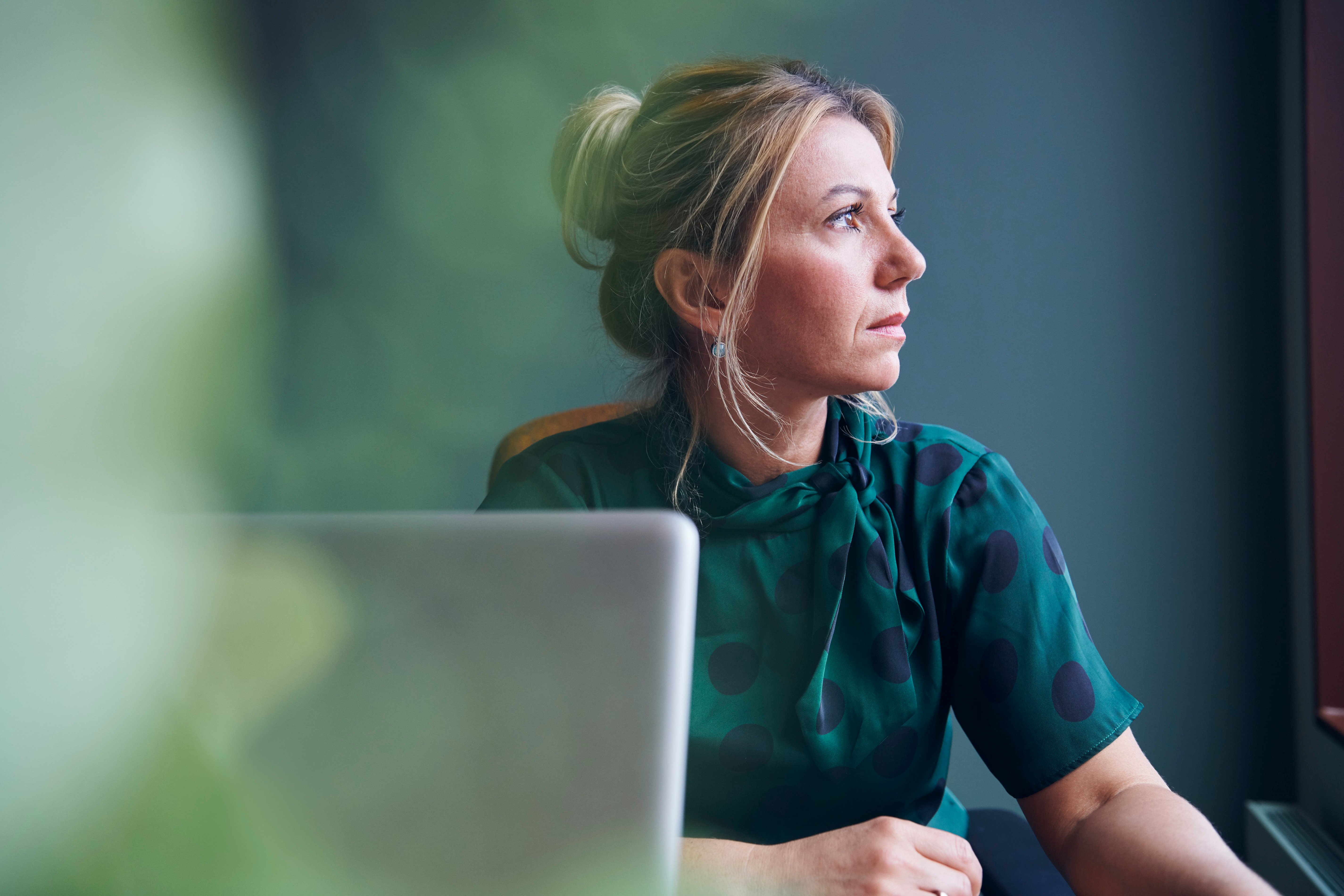 Thoughtful businesswoman looking away sitting in board room at office