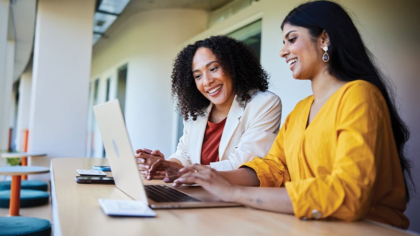 Two businesswomen smiling and working on a laptop at an office table