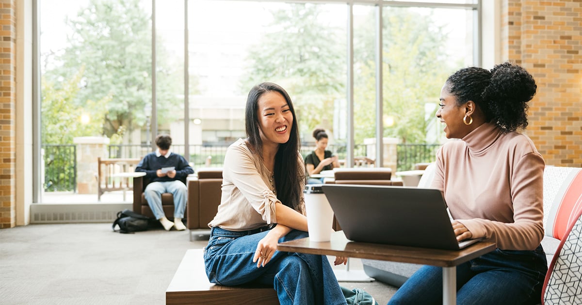 Two diverse women on laptop smiling in cafe