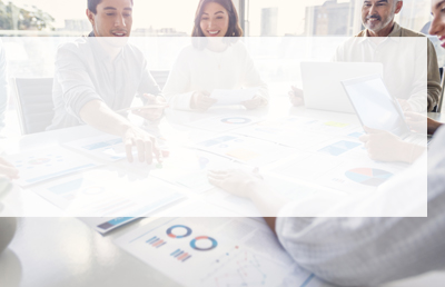 A team of workers sits around a conference table working on laptops and reviewing data and paperwork.