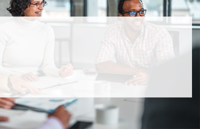 A group of people sit around a conference table engaged with a virtual webinar happening on a screen just off camera.