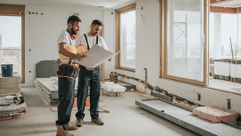Full length of construction workers analyzing blueprints in the apartment