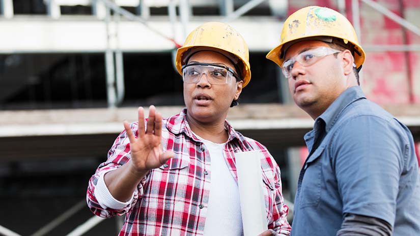 Two multi-ethnic construction workers meeting at a construction site, talking about a serious matter.