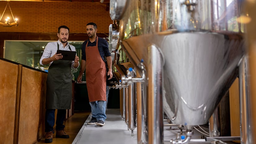 Team of men working at a brewery and controlling the production line