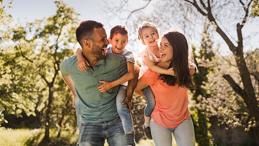 Happy parents having fun while piggybacking their small kids in nature