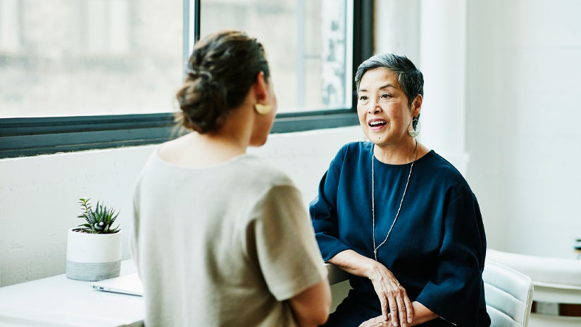 Two mature business women speaking to each other.