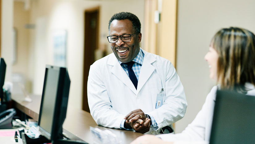 African american male doctor talking to nurse at nurse station. 