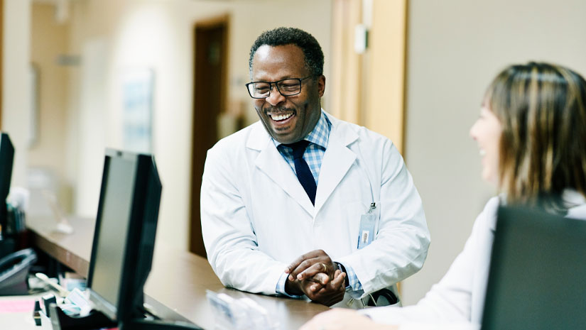 African american male doctor talking to nurse at nurse station.