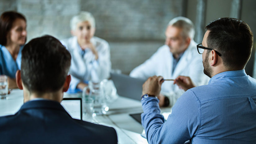 Rear view of businessmen having a business meeting with team of doctors at doctor's office. Focus is on man on the right.