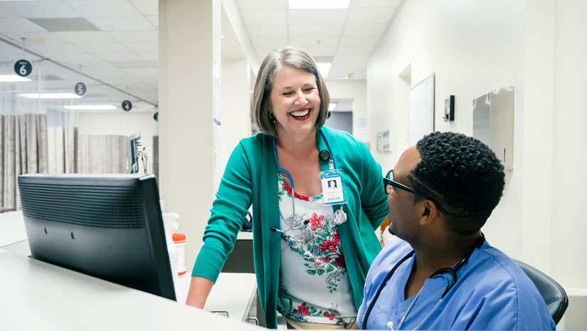 Two female nurses laughing behind nurse's desk.