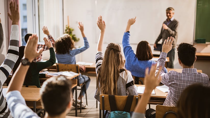 Back view of high school students raising hands on a class