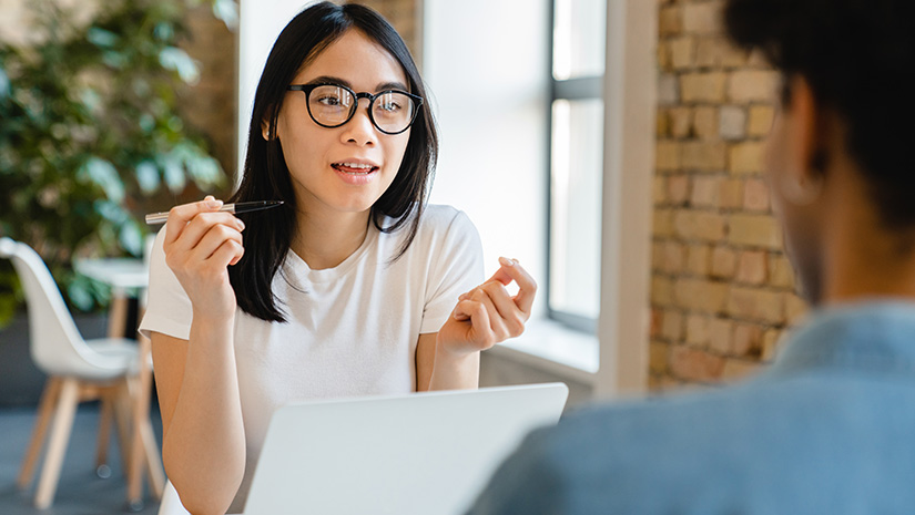 Confident young businesswoman talking with her colleague at the working desk