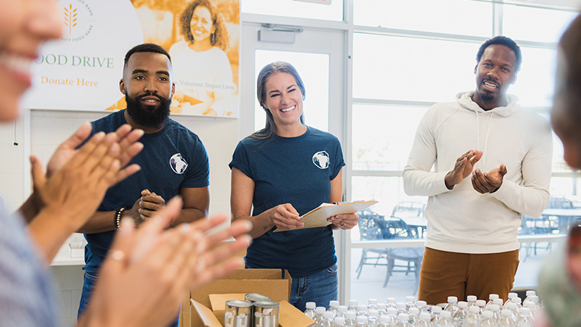 Food drive volunteers clap and smile at unseen person
