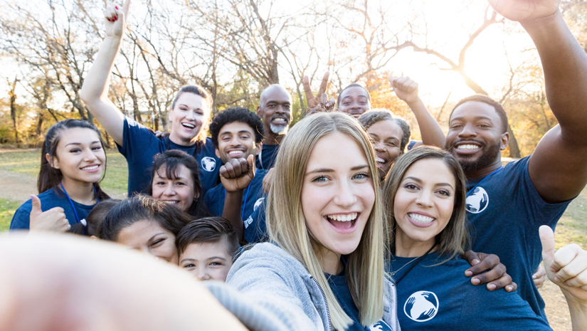 Young woman takes a selfie with a group of friends who are participating in a community cleanup event.