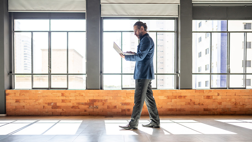 Mature businessman walking and using laptop at office