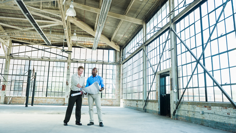 Two realtors looking at construction plans in empty building.