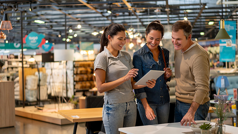 Cheerful sales woman showing a design on tablet to mid adult couple looking