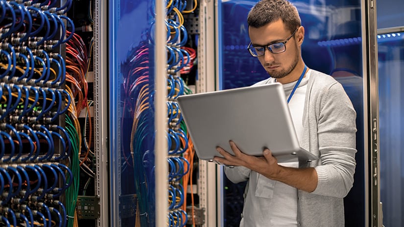 Young man holding laptop standing in server room