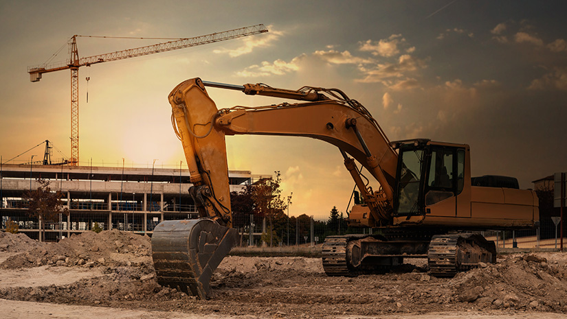A large excavator at a construction site with cranes and scaffolding