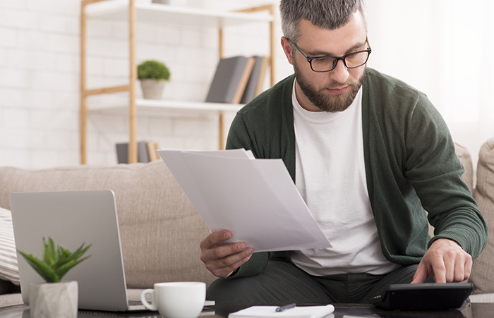 Man with calculator counting money and checking bills online